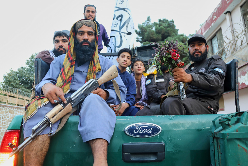 En beväpnad taliban och andra sitter på flaket till en jeep.
