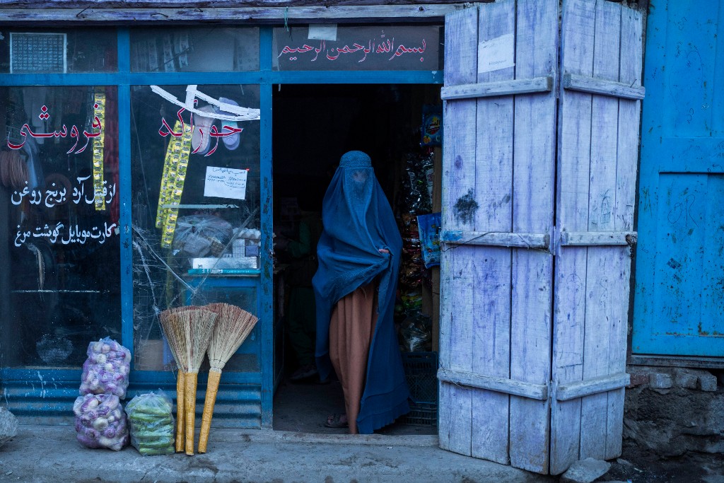 Kvinna i blå burqa står i dörröppningen till en affär.