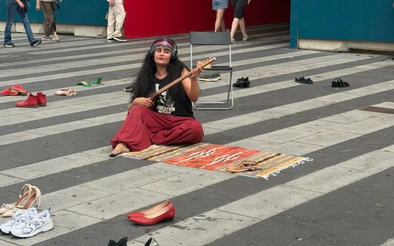 Morvarid Sahel sitter på gatan och spelar på instrument under manifestation.