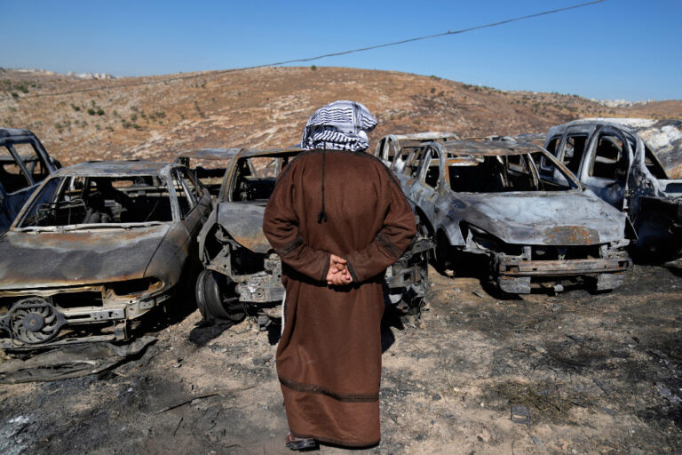 Man med palestinasjal på huvudet ser ut över utbrända fordon.